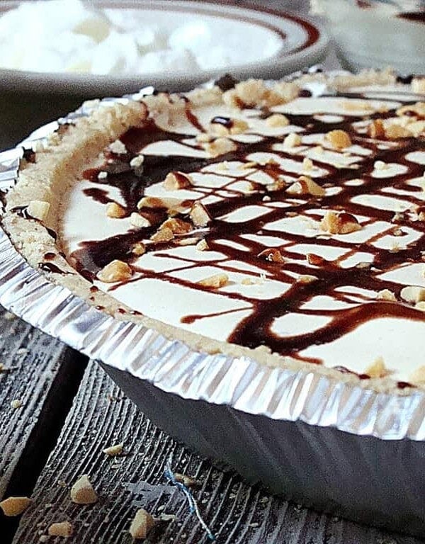 A side shot of a peanut butter pie topped with a drizzle of chocolate sauce.
