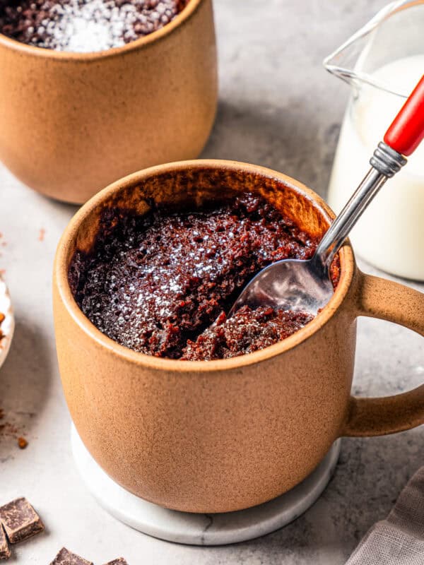 A spoon in a chocolate mug cake, with a second mug cake in the background.