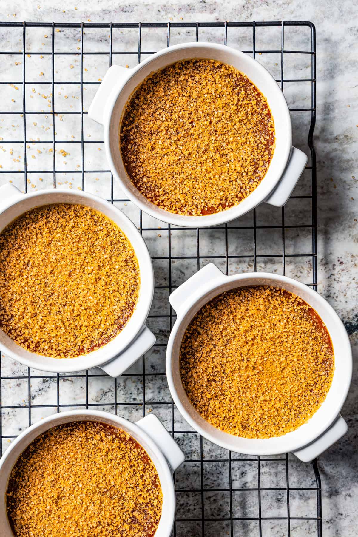 Coffee crème brûlée topped with sugar in ramekins cooling on a wire rack.