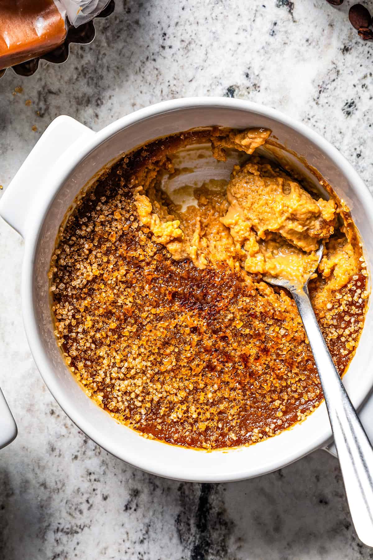 Close-up view of a spoon resting in a ramekin of coffee crème brûlée.