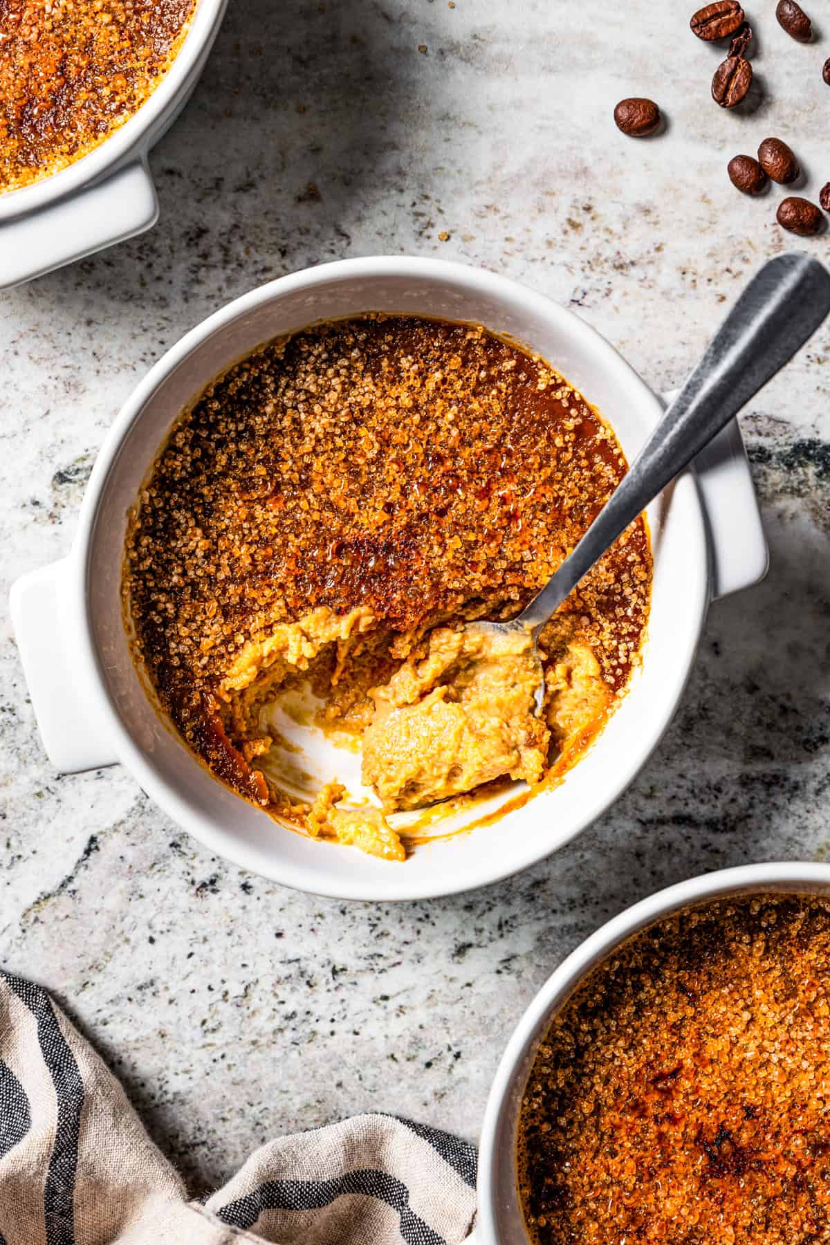 Overhead view of a spoon resting in a ramekin of coffee crème brûlée.