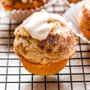 a side shot of an apple pie muffins resting on a black wire rack surrounded with more muffins