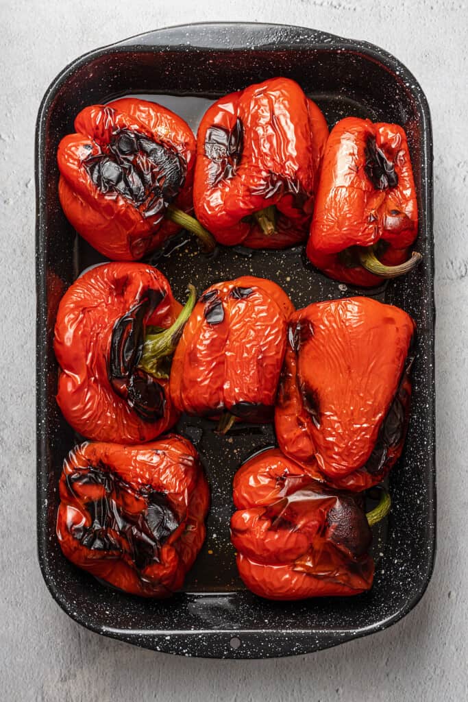 Whole roasted red peppers on a metal baking pan.