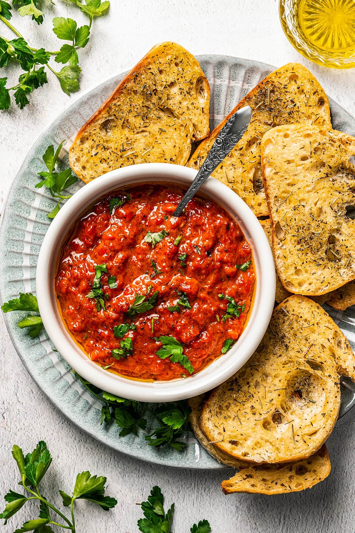 A bowl of Ajvar served on a plate surrounded by bread slices.