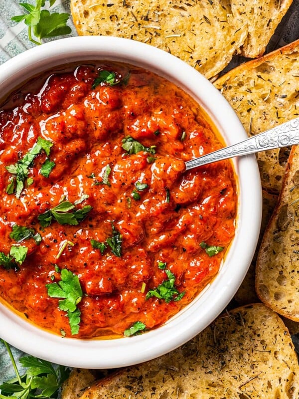 A bowl of Ajvar served on a plate surrounded by bread slices.