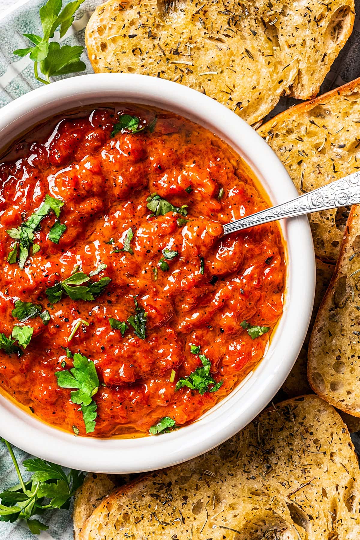 A bowl of Ajvar served on a plate surrounded by bread slices.