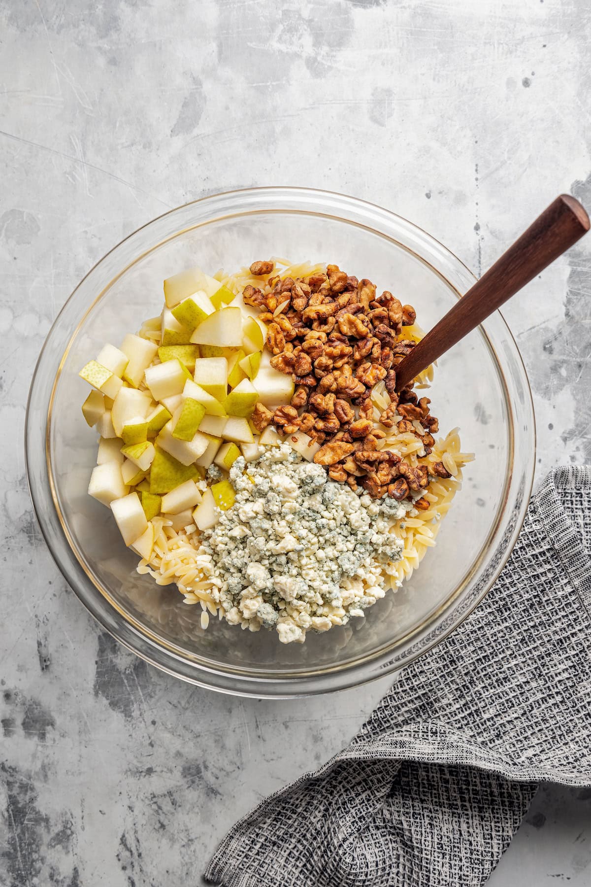 Orzo, walnuts, pears, and gorgonzola cheese combined in a glass bowl.