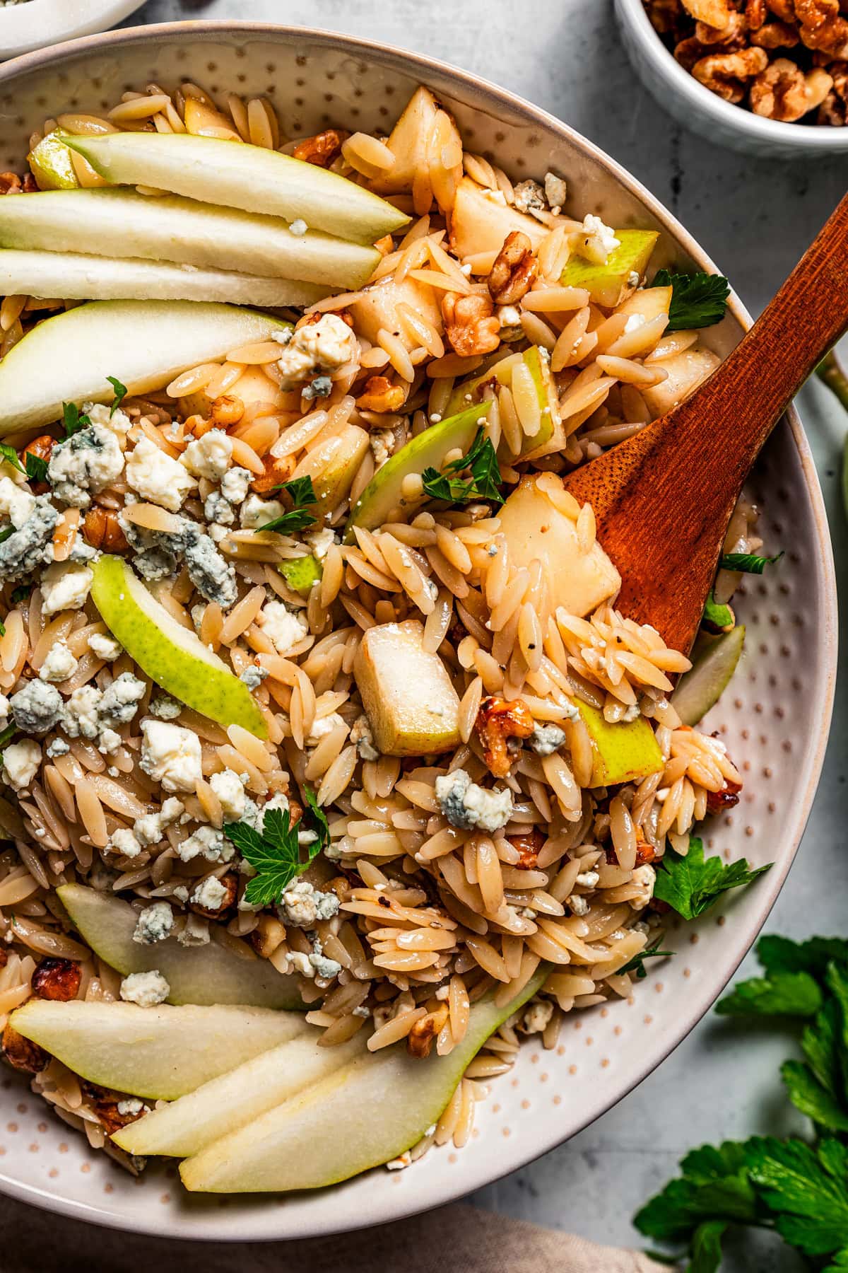Orzo in a bowl and garnished with sliced pears, chopped nuts, and cheese.