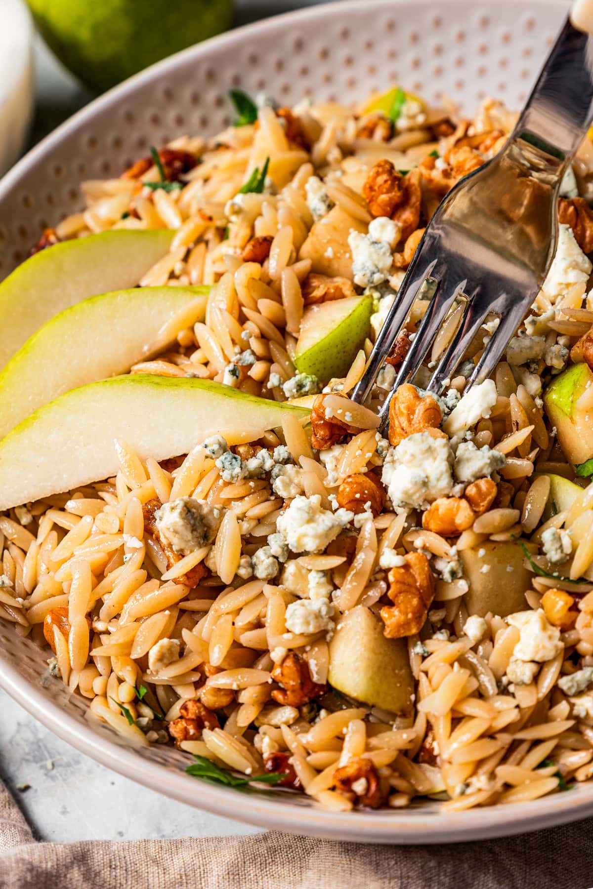 A fork in orzo pasta tossed with chunks of pears and chopped nuts.