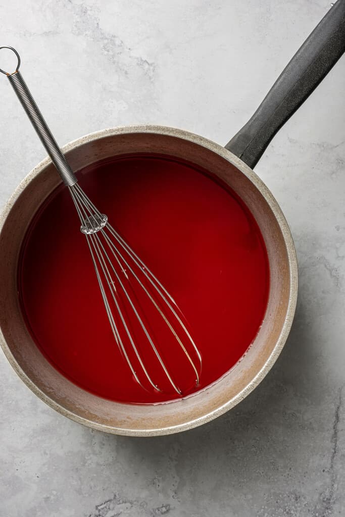 Overhead view of red Jell-O mixture in a pot with a whisk