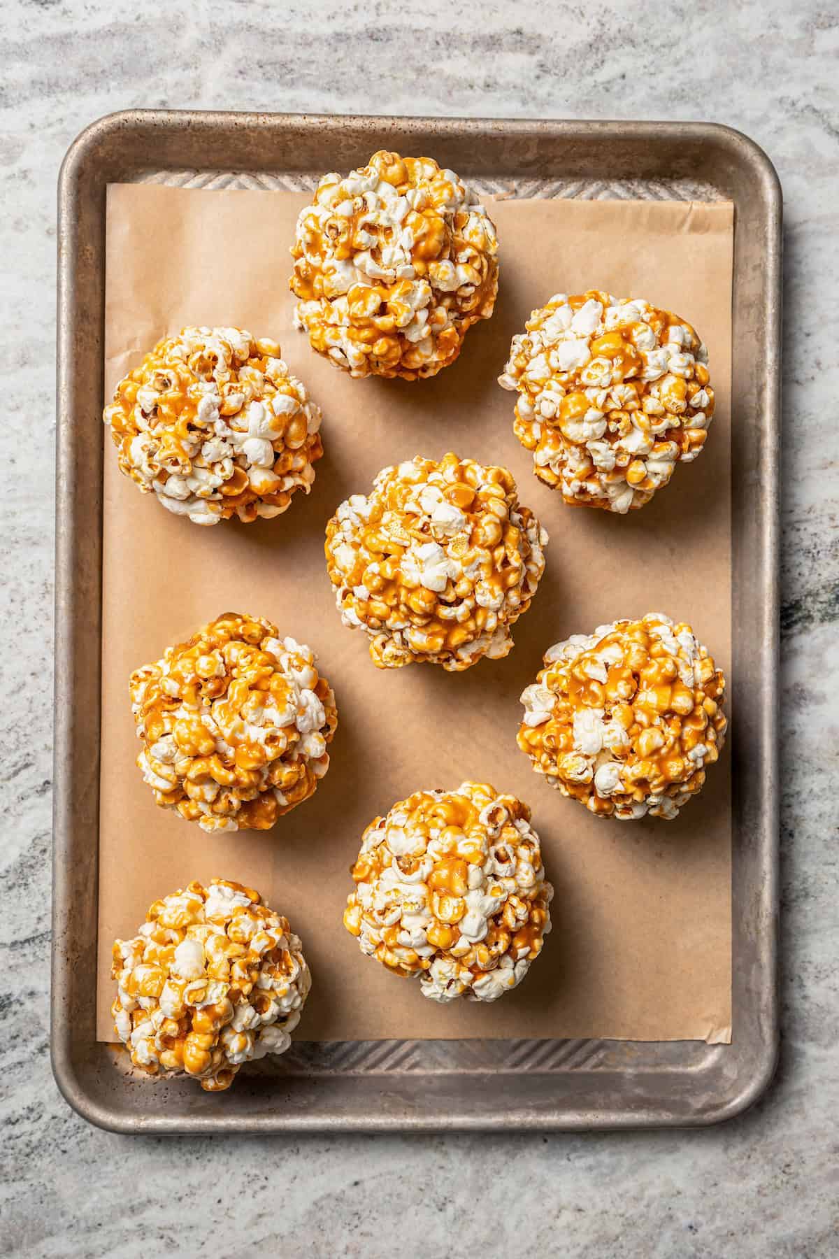 Overhead view of caramel popcorn balls on a parchment-lined baking sheet.