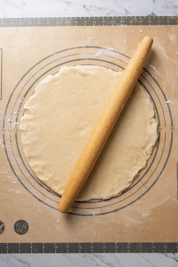 Overhead view of a piece of pie crust dough being rolled out, with a rolling pin on it
