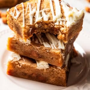 Three blondies stacked on a white plate with a bite missing from the top blondie.