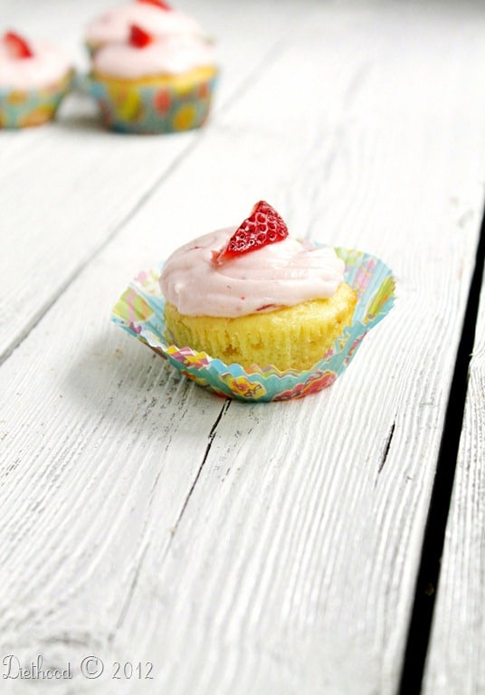 A yogurt cupcake with strawberry cream cheese frosting being peeled out of a cupcake wrapper.