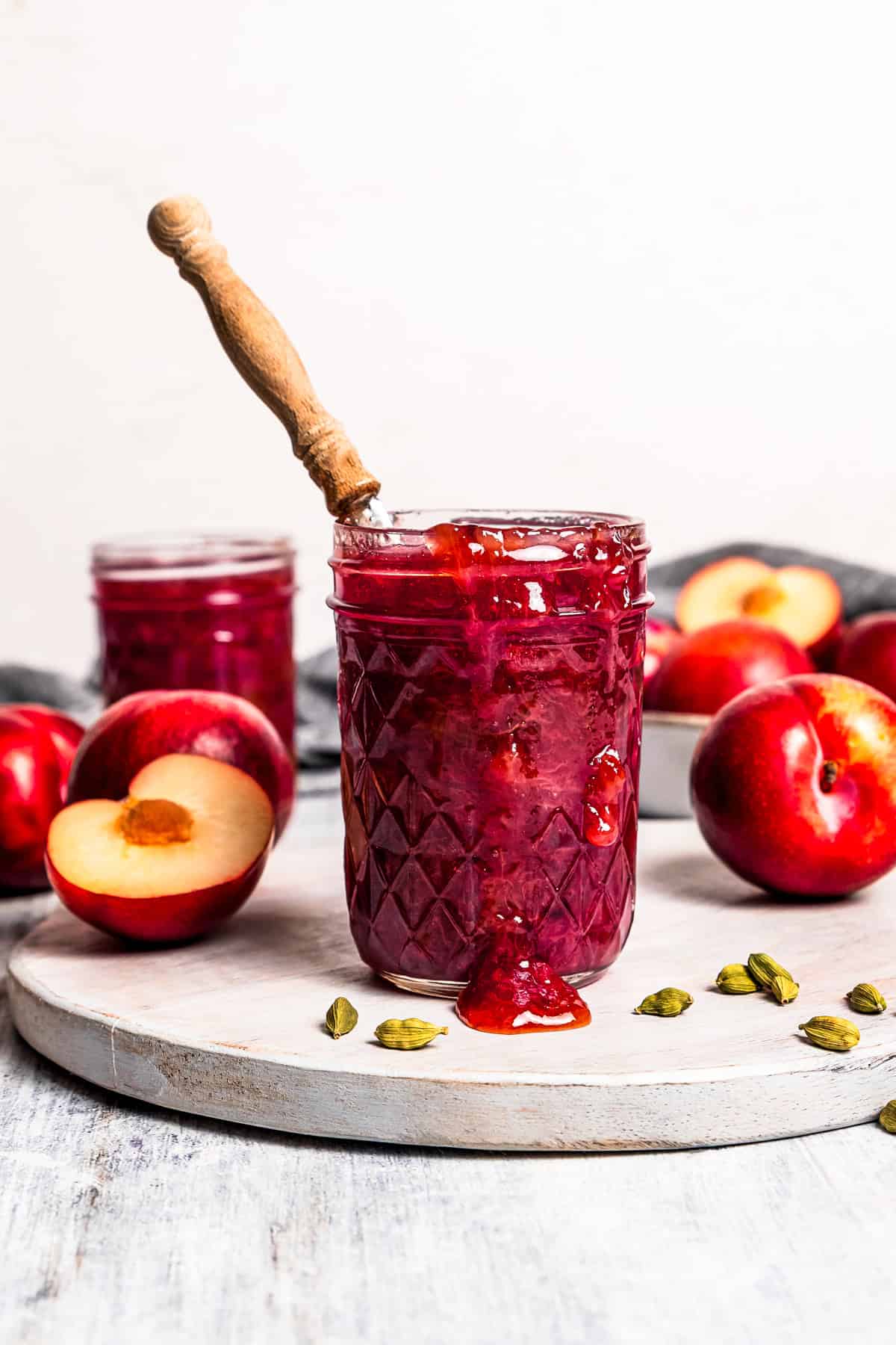 A spoon in a jar of plum jam with fresh plums in the background.