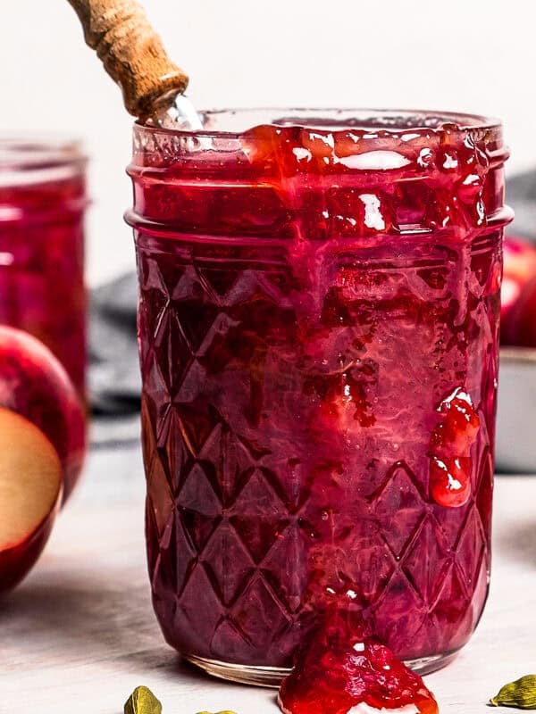 A wide angle of plum jam in jars, with fresh plums set around the jars.