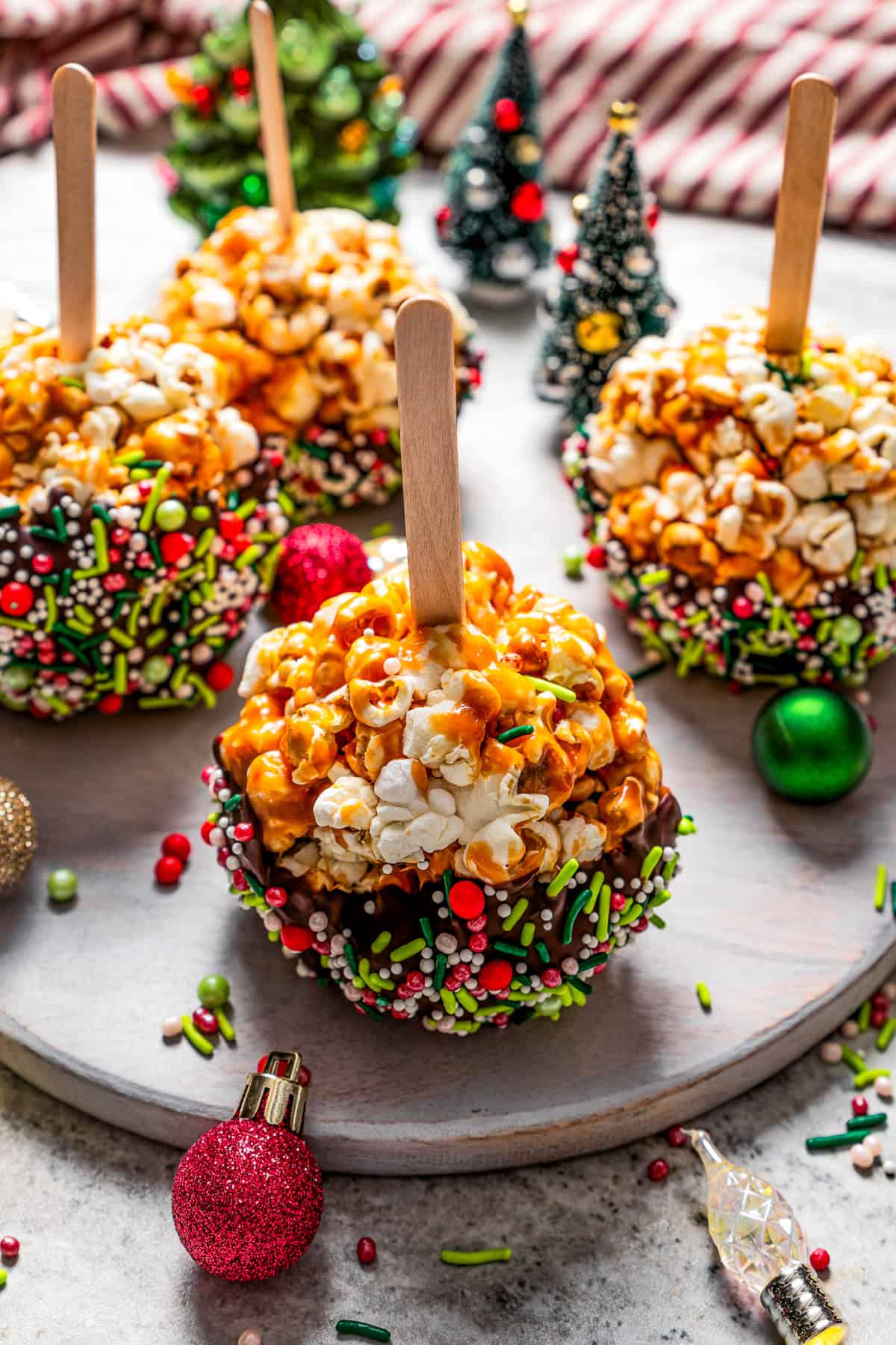 Chocolate-dipped caramel popcorn balls on popsicle sticks and arranged on a round platter.