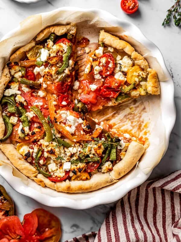 Overhead view of a tomato tart on a serving dish, with two slices cut out, and one on the dish.