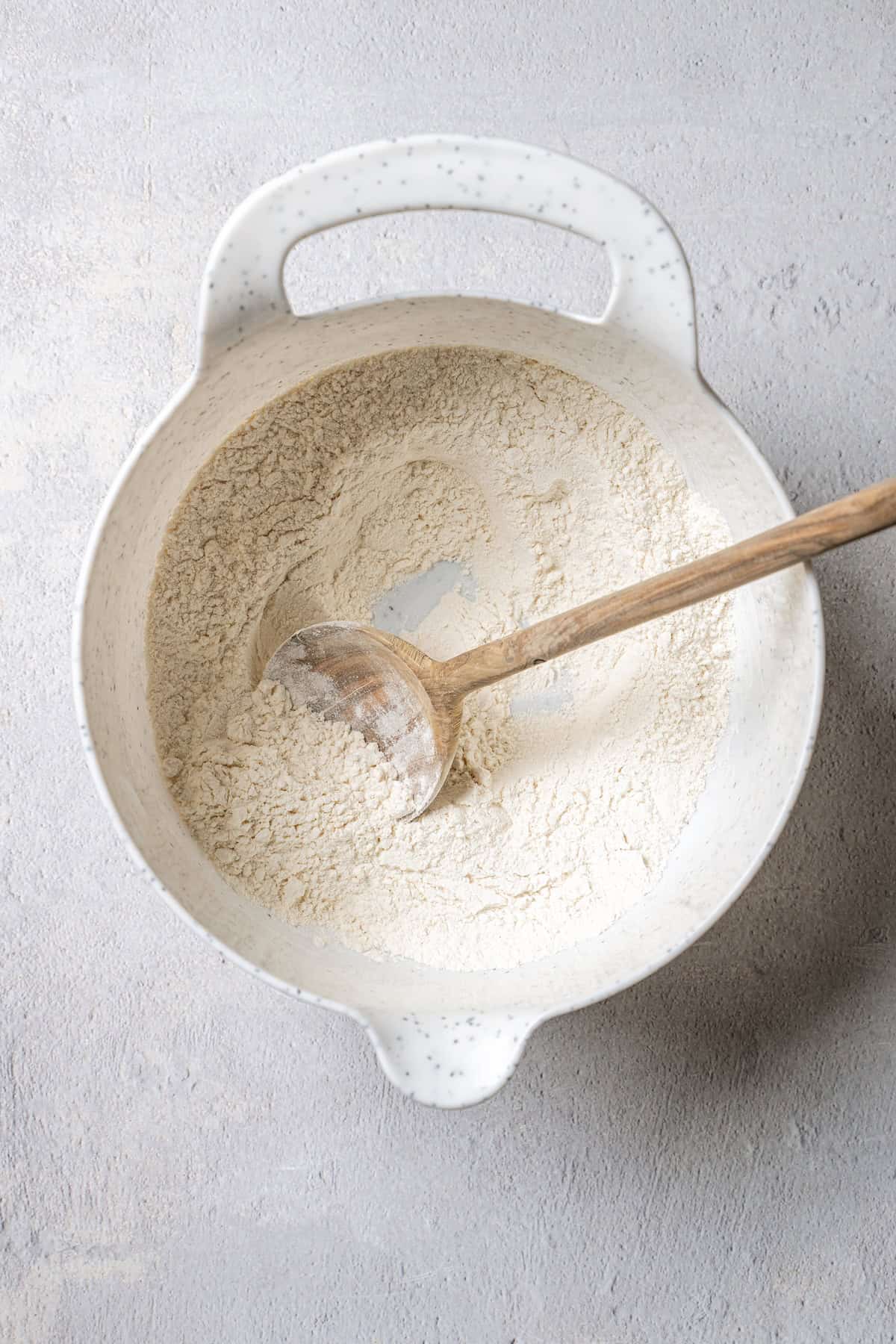 Dry ingredients combined in a plastic bowl with a wooden spoon.