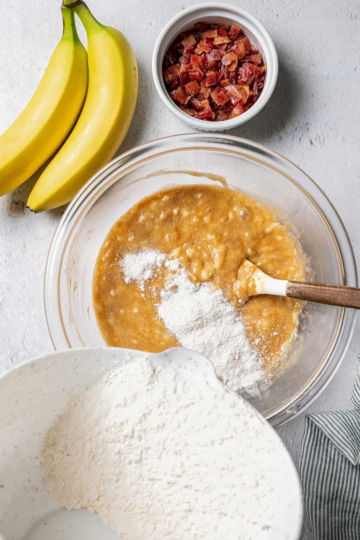 Dry ingredients being added to wet ingredients in a glass mixing bowl.