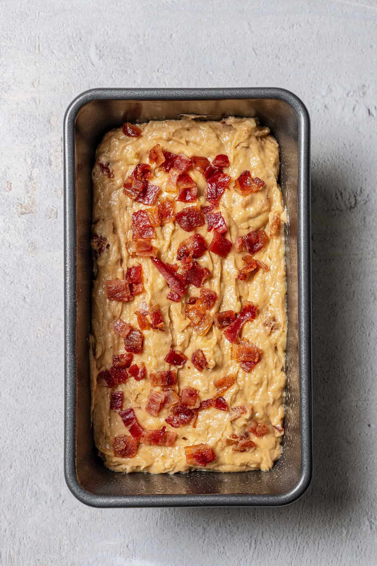 Peanut butter banana bread batter topped with crumbled candied bacon in a loaf pan.