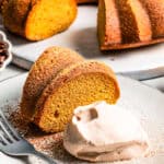 A slice of pumpkin cake served on a plate with a dollop of espresso whipped cream set next to the cake.