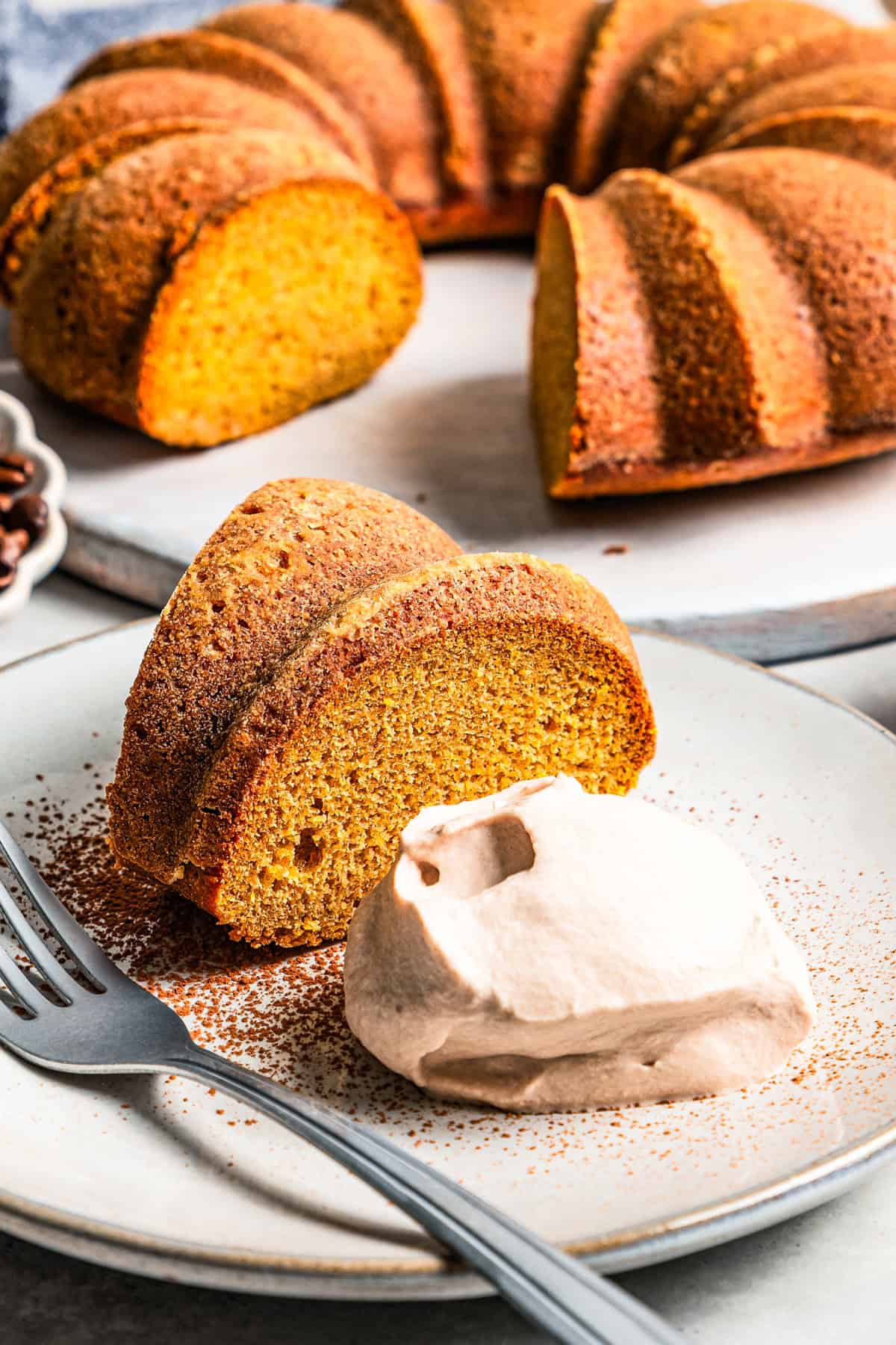 A slice of pumpkin cake served on a plate with a dollop of espresso whipped cream set next to the cake.