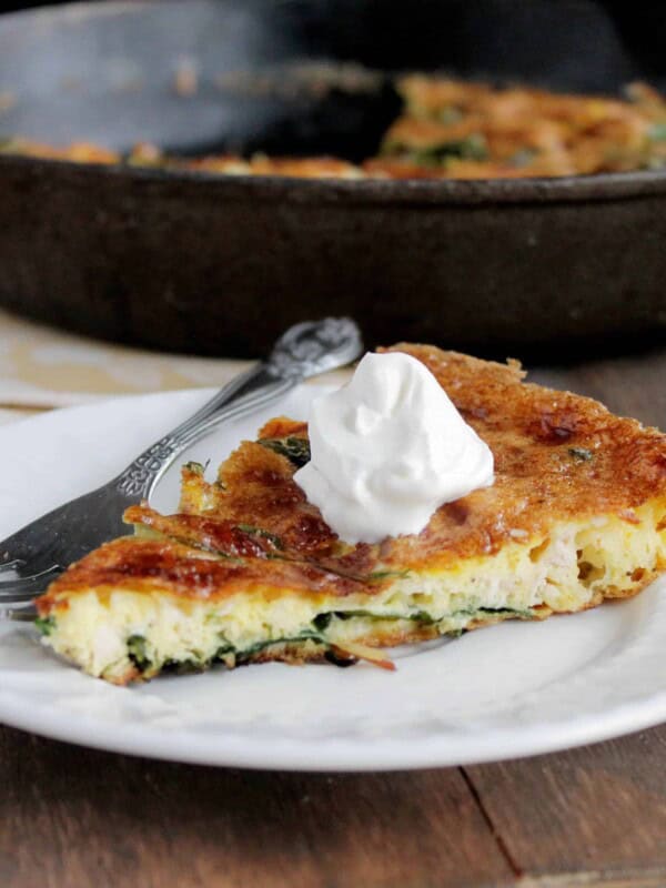A slice of leftover turkey frittata topped with sour cream, with the skillet in the background