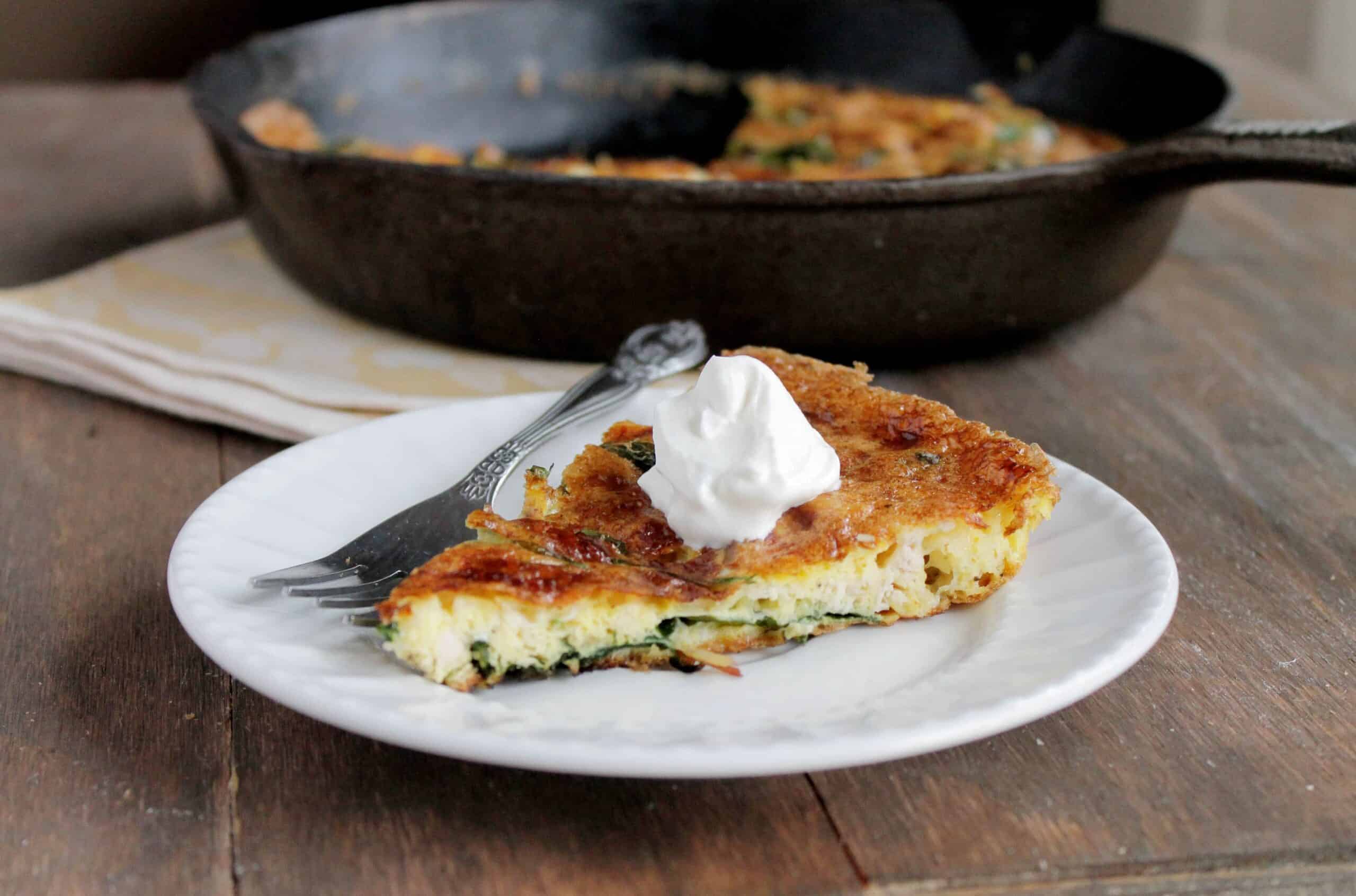 A slice of leftover turkey frittata topped with sour cream, with the skillet in the background.
