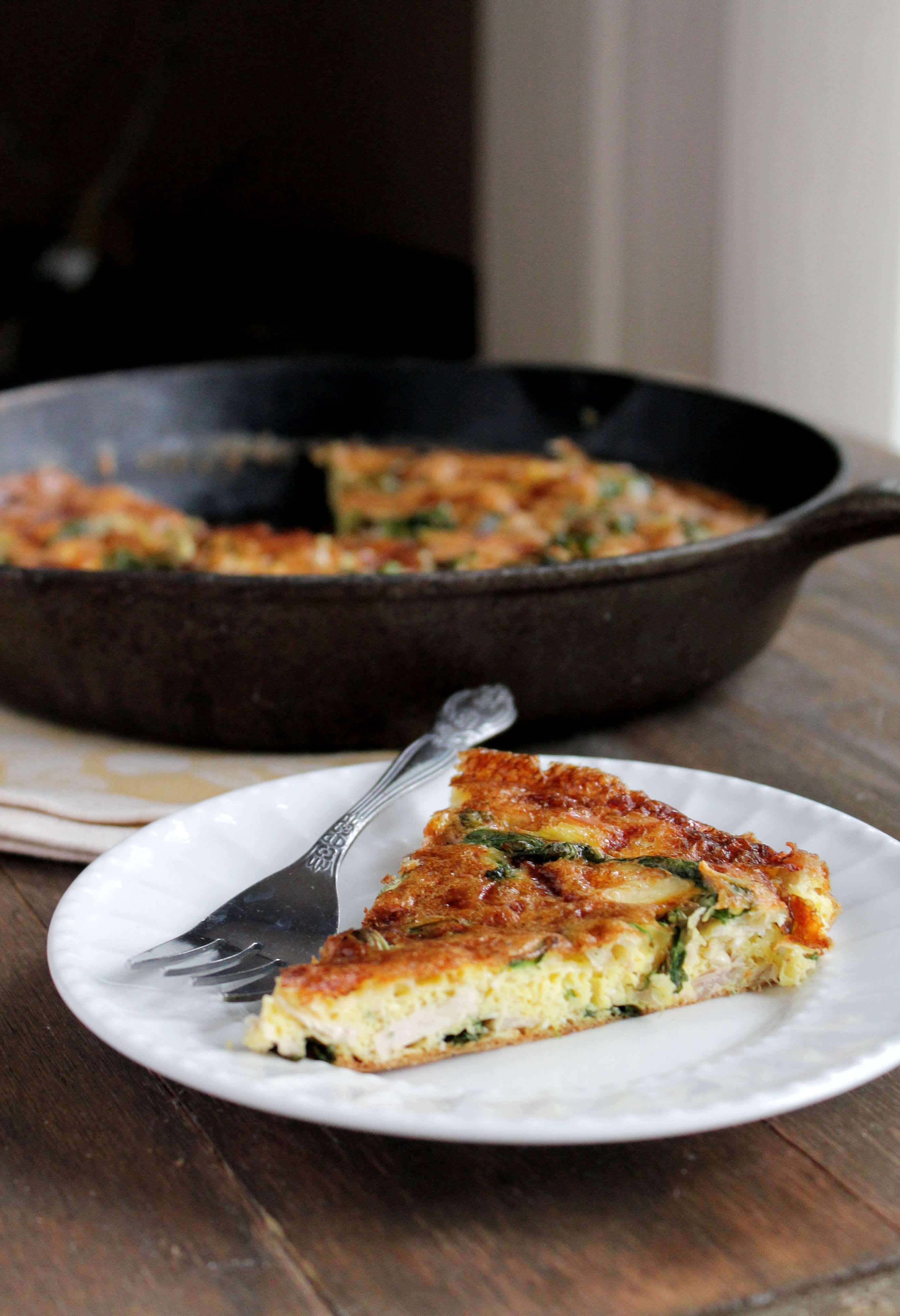 A slice of turkey frittata filled with spinach and mozzarella cheese on a plate, with the skillet in the background