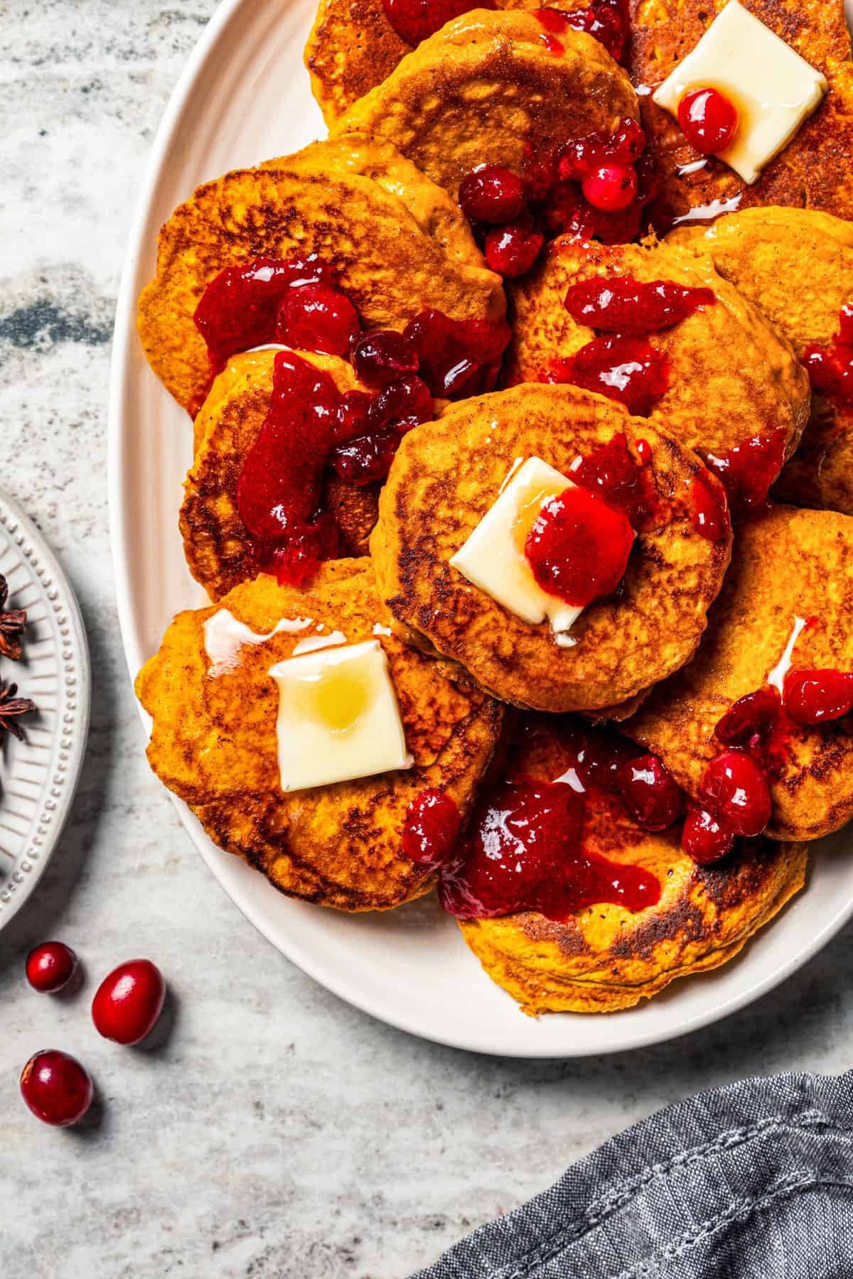 Pumpkin pancakes are the best fall breakfast! Made from pancake mix, real pumpkin, and spices, topped with cranberry syrup for the holidays. Pumpkin pancakes served on a large platter.