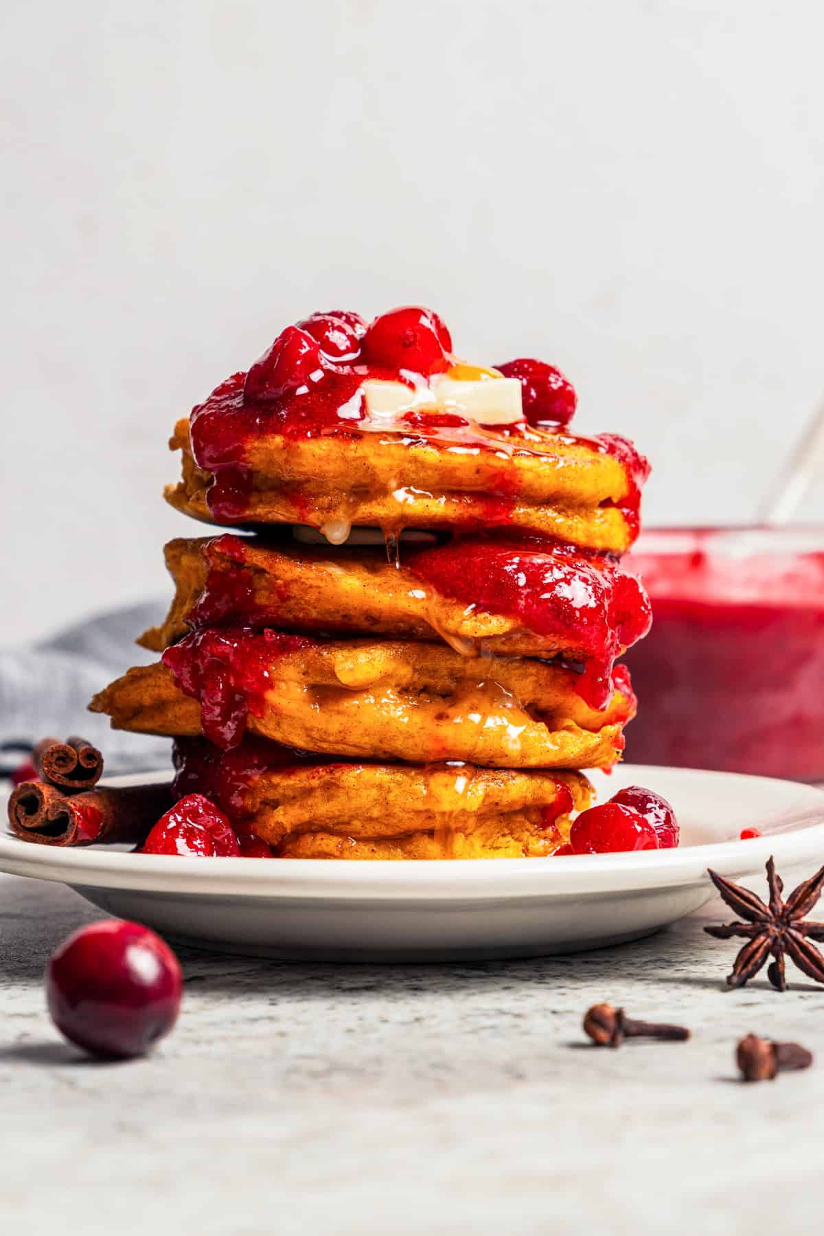 Pumpkin pancakes are the best fall breakfast! Made from pancake mix, real pumpkin, and spices, topped with cranberry syrup for the holidays. A stack of pumpkin pancakes topped with cranberry sauce.