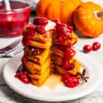 A tall stack of pumpkin pancakes topped with cranberry maple syrup on a plate.