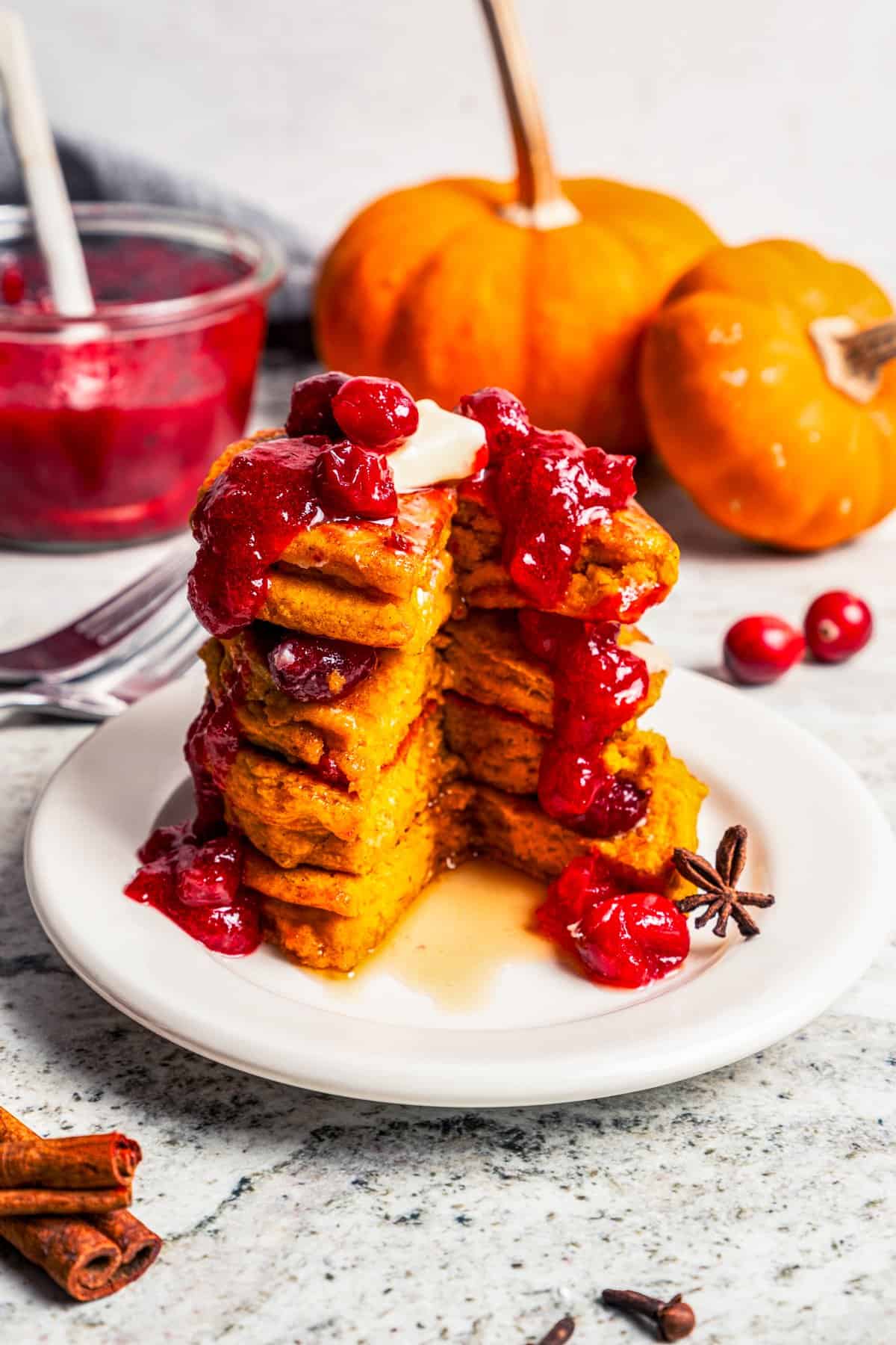 Pumpkin pancakes are the best fall breakfast! Made from pancake mix, real pumpkin, and spices, topped with cranberry syrup for the holidays. A tall stack of pumpkin pancakes topped with cranberry maple syrup on a plate.