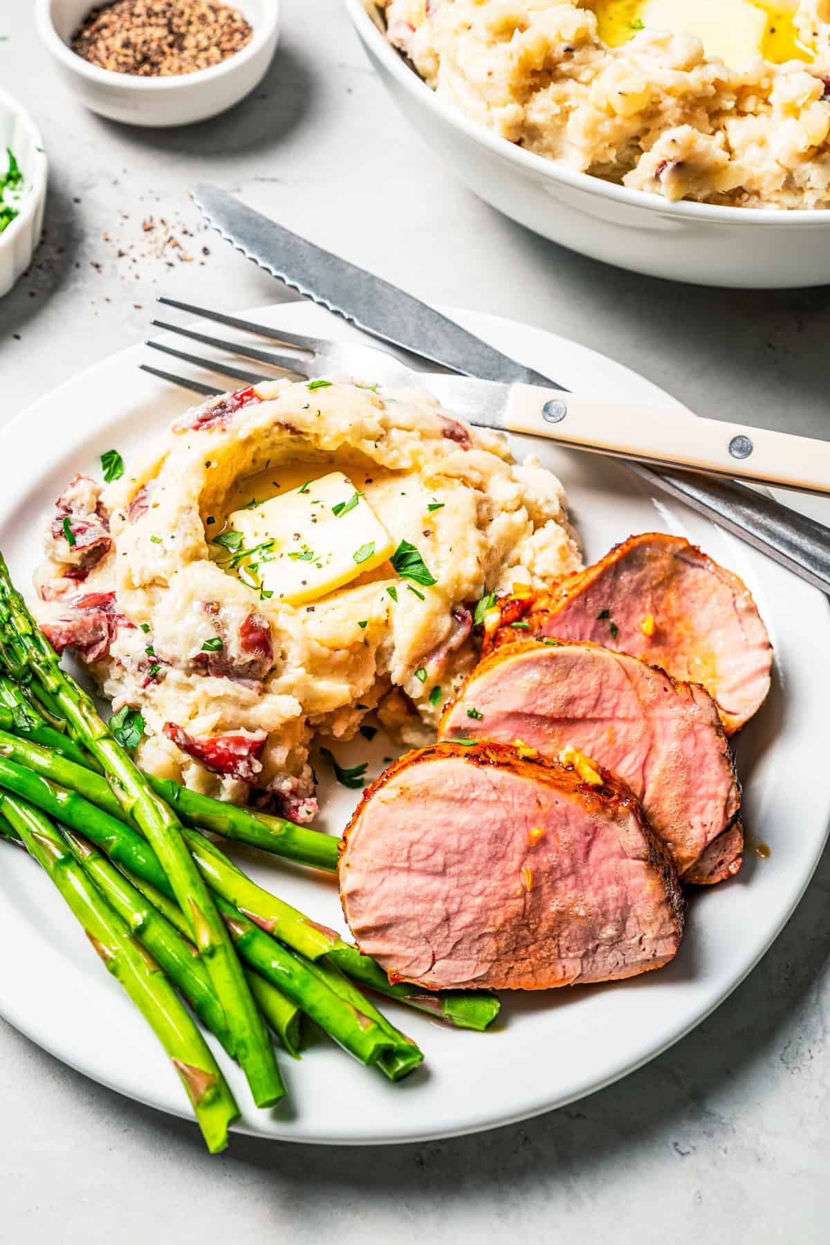 These slow cooker garlic mashed potatoes are made with creamy, skin-on red potatoes and plenty of butter! No boiling, and only 6 ingredients. Country garlic mashed potatoes served next to pork chops and asparagus on a plate.