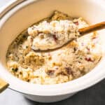 A wooden spoon scooping country garlic mashed potatoes from the slow cooker.