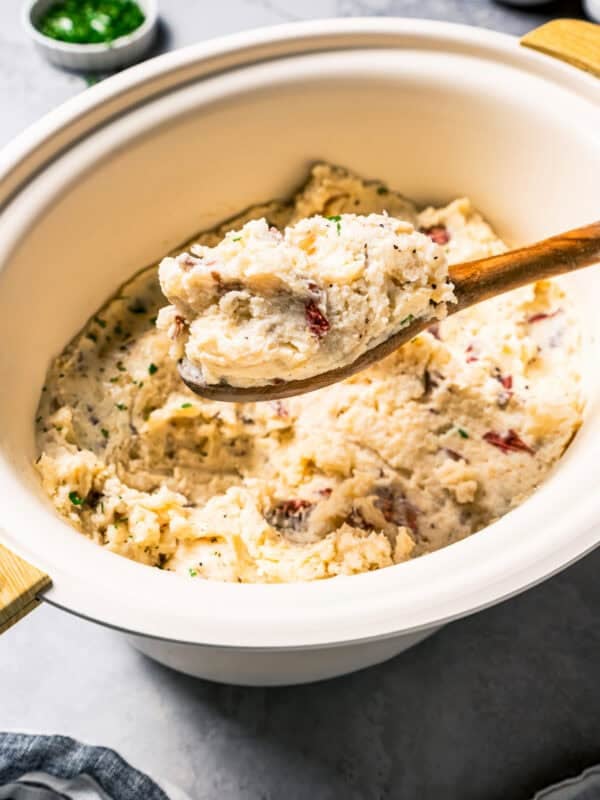 A wooden spoon scooping country garlic mashed potatoes from the slow cooker.