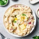 A bowl of mashed potatoes topped with pats of butter.