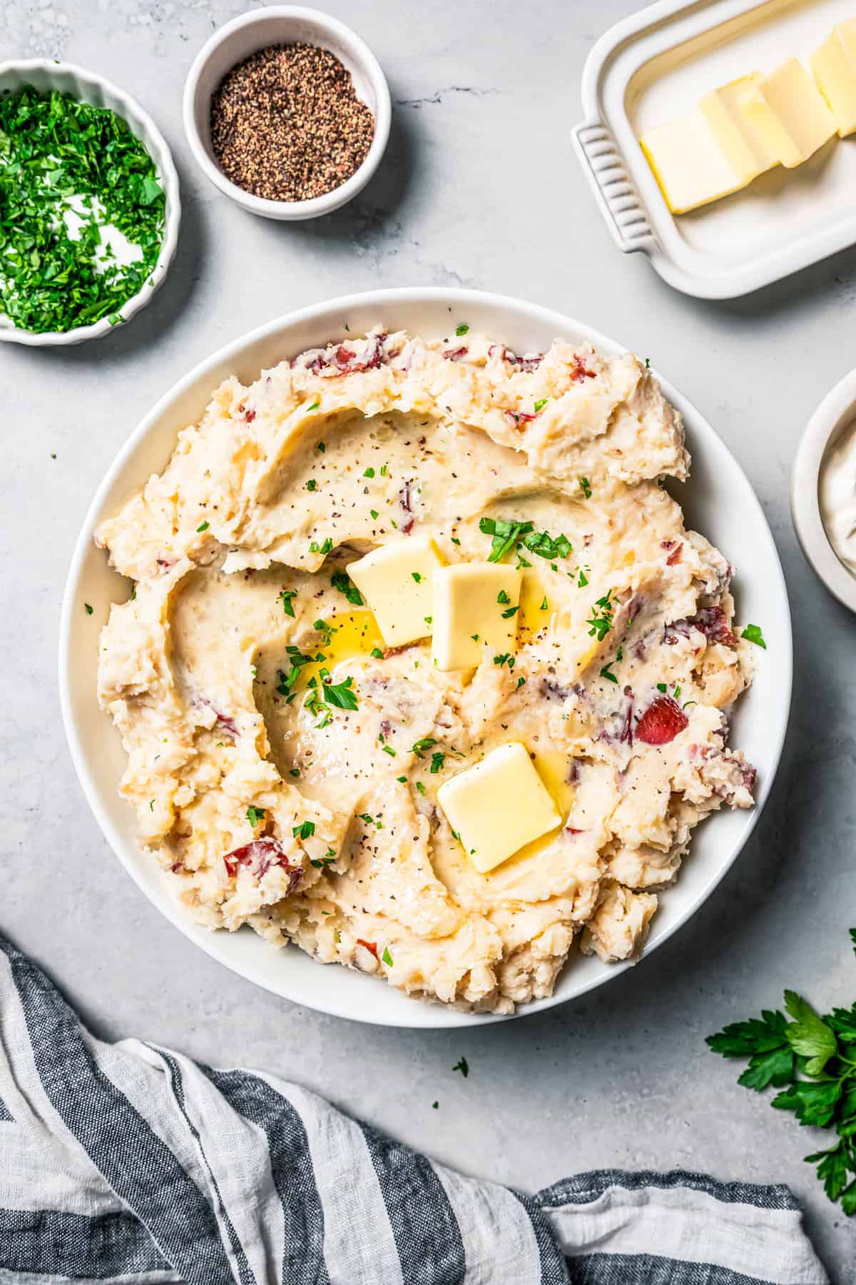 These slow cooker garlic mashed potatoes are made with creamy, skin-on red potatoes and plenty of butter! No boiling, and only 6 ingredients. A bowl of mashed potatoes topped with pats of butter.