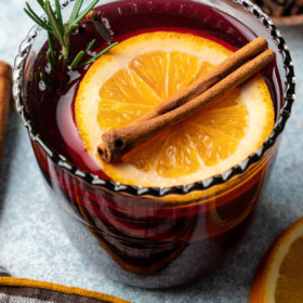 Mulled wine served in a glass garnished with an orange slice and a cinnamon stick.