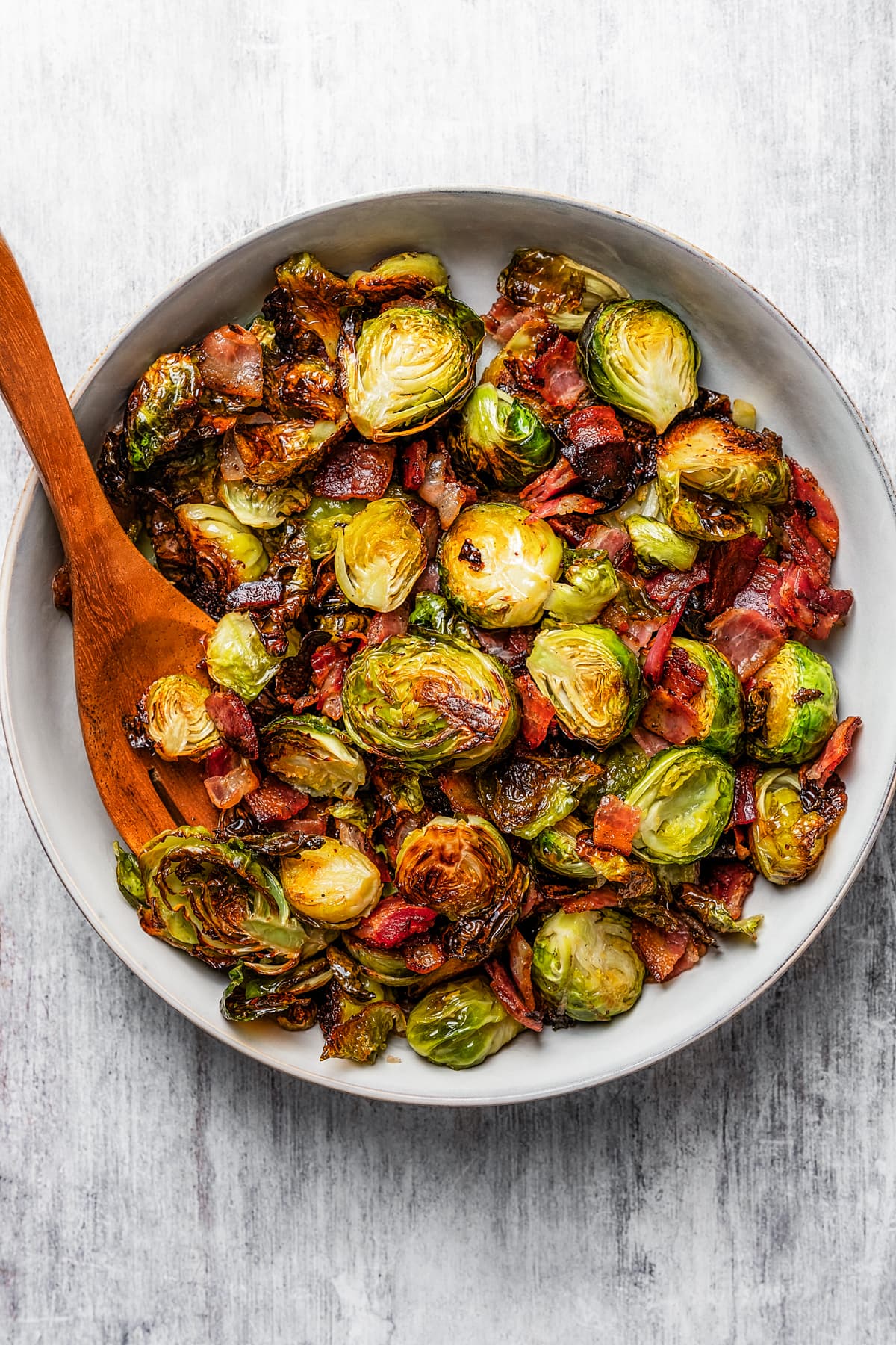 Roasted Brussels sprouts and bacon in a serving bowl with a wooden serving fork.