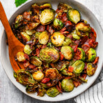 Roasted Brussels sprouts and bacon in a serving bowl with a wooden serving fork.