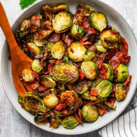 Roasted Brussels sprouts and bacon in a serving bowl with a wooden serving fork.
