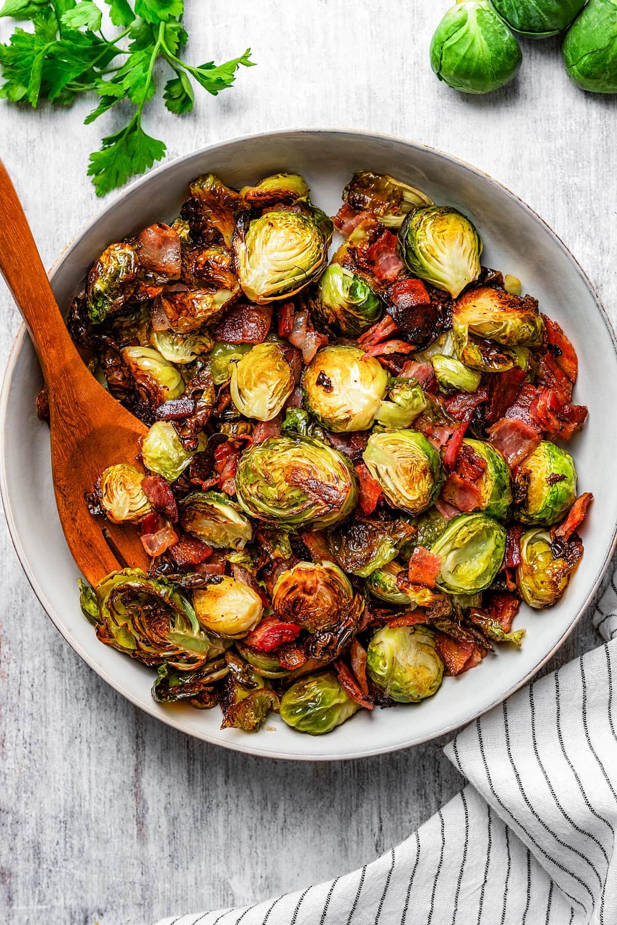 Roasted Brussels sprouts and bacon in a serving bowl with a wooden serving fork.