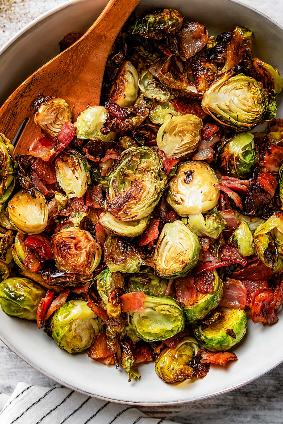 Scooping roasted Brussels sprouts and bacon from a serving bowl with a wooden serving fork.
