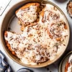 Frosted cinnamon rolls topped with pecans in a round baking pan, with one cinnamon roll missing.