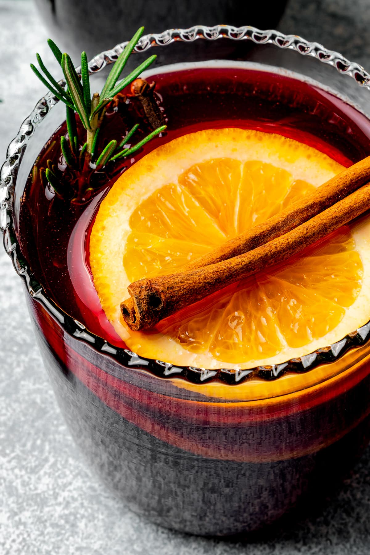 Close-up image of Mulled wine served in a glass garnished with an orange slice and a cinnamon stick.
