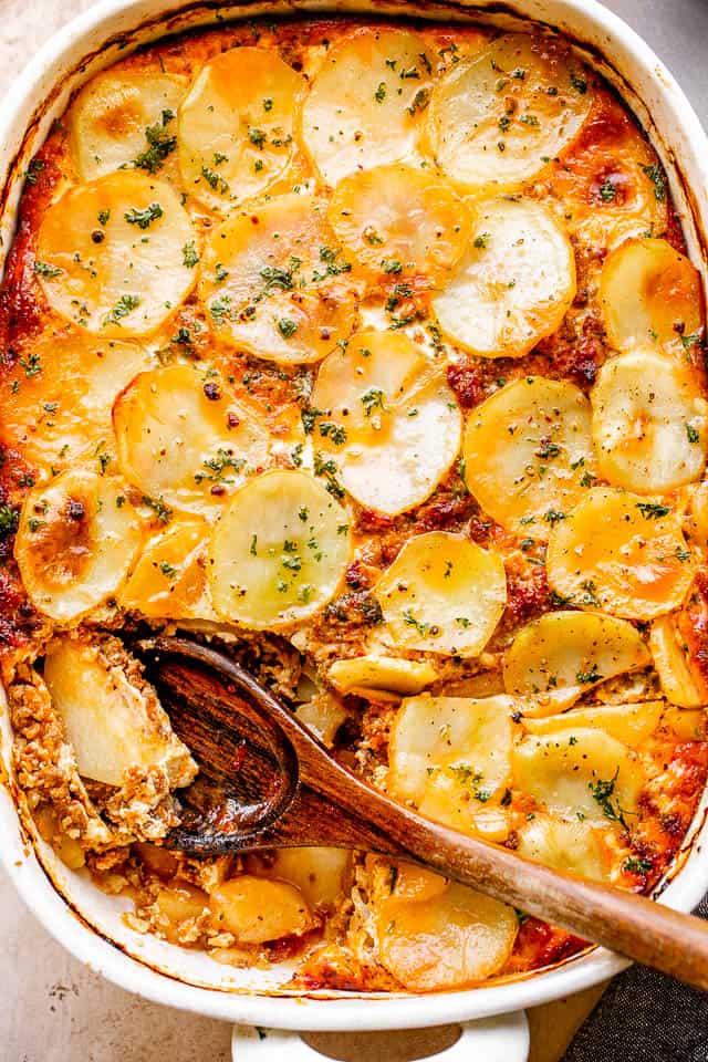 Overhead view of Macedonian moussaka in a casserole dish with a wooden serving spoon.