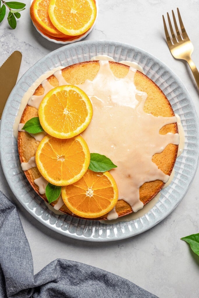 Overhead view of glazed olive oil cake on a plate, garnished with orange slices and mint leaves.