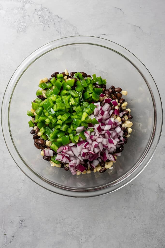 Overhead view of a pile of green bell pepper and a pile of red onion on top of corn and black beans